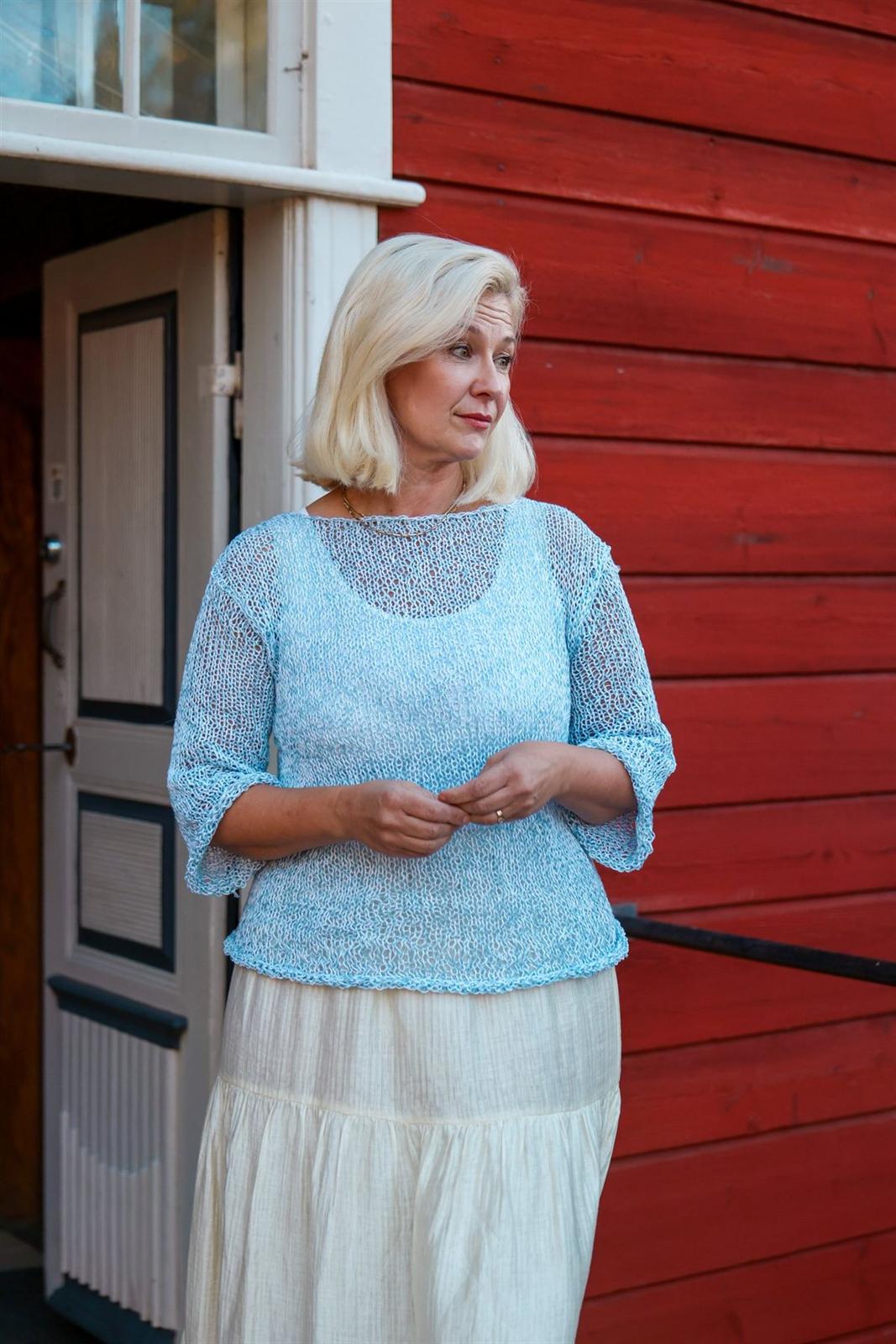 Gita Yli-Hannuksela punaisen hirsiseinän edessä