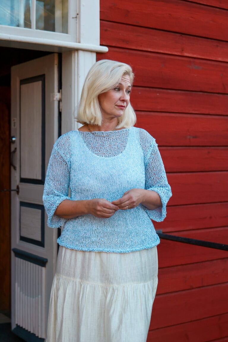 Gita Yli-Hannuksela punaisen hirsiseinän edessä